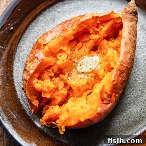 Close up shot of a cut open baked sweet potato topped with melted butter on a plate