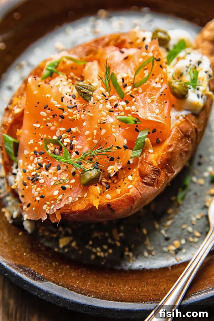 Close up shot of a baked sweet potato on a plate topped with sour cream, smoked salmon and capers, garnished with dill.