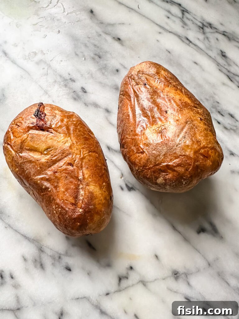 Top down shot of two perfectly baked potatoes resting on a sleek marble counter, ready to be topped.