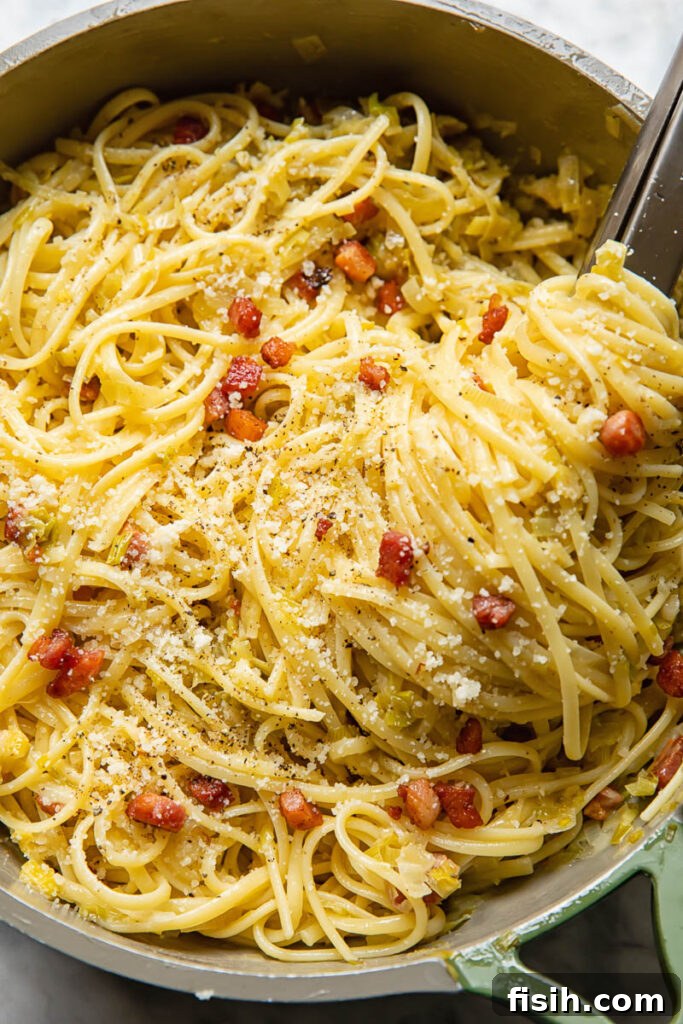 Close-up of a pan filled with creamy leek and pancetta pasta, featuring cooking tongs for serving.