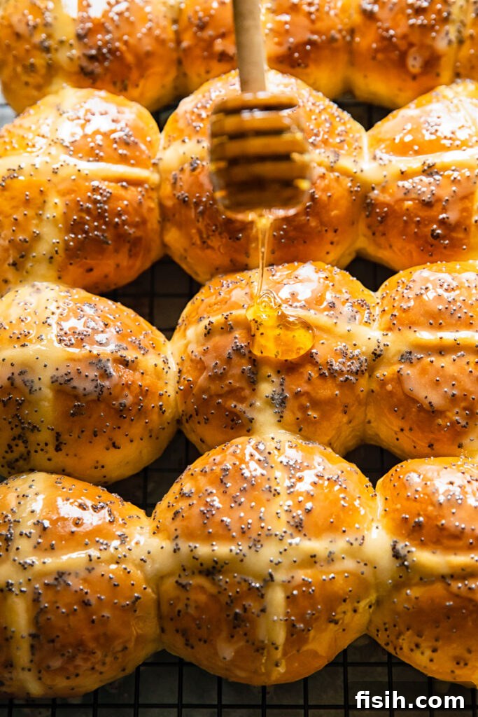 Sunshine Lemon Poppy Seed Hot Cross Buns 2 Golden-brown lemon poppyseed hot cross bun being drizzled generously with a sweet, glossy honey glaze, signifying the final delicious touch.