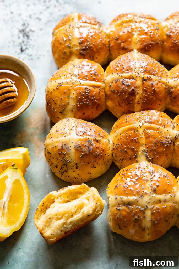 Sunshine Lemon Poppy Seed Hot Cross Buns 3 Close-up view of freshly baked lemon poppyseed hot cross buns, one split open to reveal its fluffy, tender crumb and hints of poppyseeds inside.