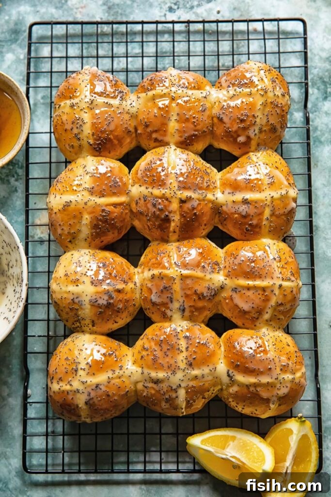 Sunshine Lemon Poppy Seed Hot Cross Buns 5 Freshly glazed lemon poppyseed hot cross buns cooling on a wire rack, garnished with vibrant lemon slices, ready to be enjoyed.