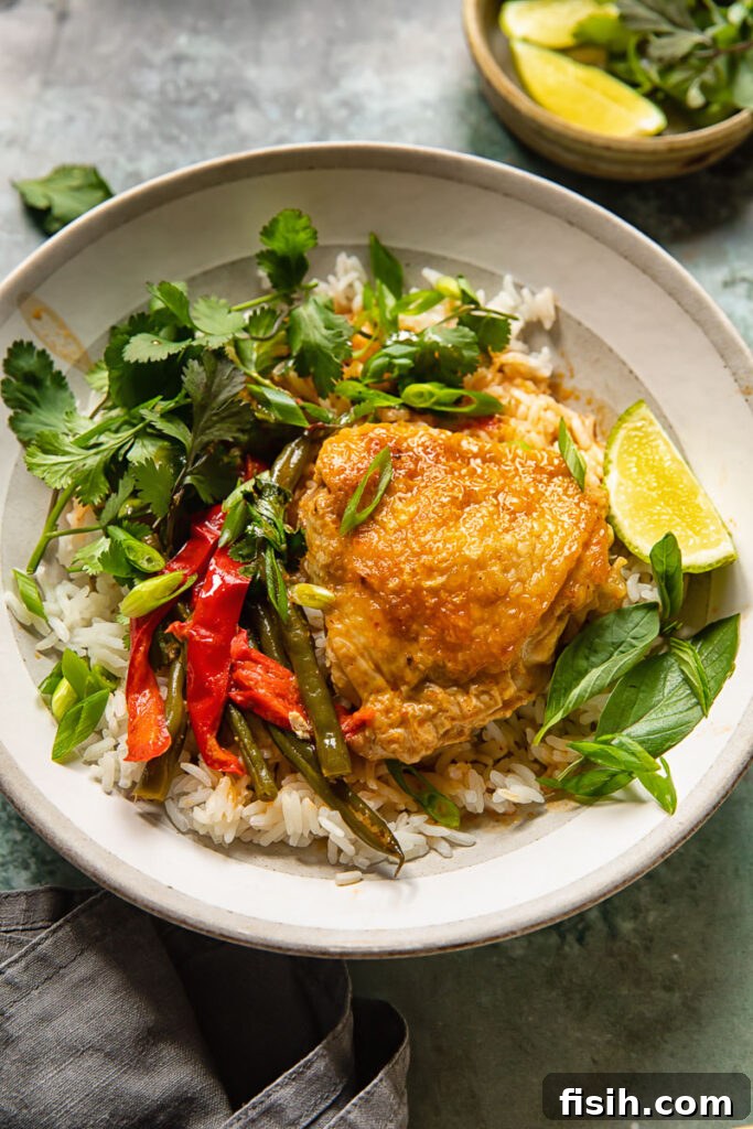 A bowl of coconut curry with a chicken thigh and white rice