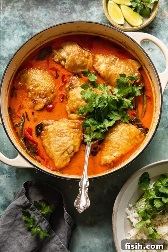 Pan of braised coconut curry with chicken thighs, a serving spoon, and fresh parsley