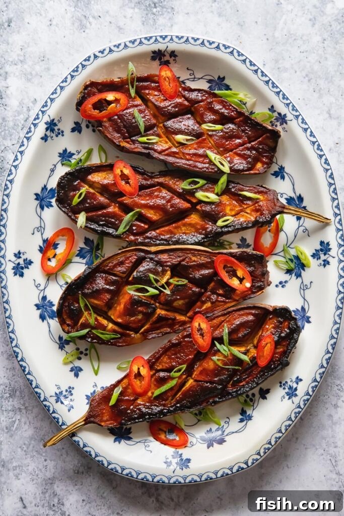 Top-down view of a plate featuring four pieces of miso-glazed aubergine, garnished with sesame seeds and fresh herbs.