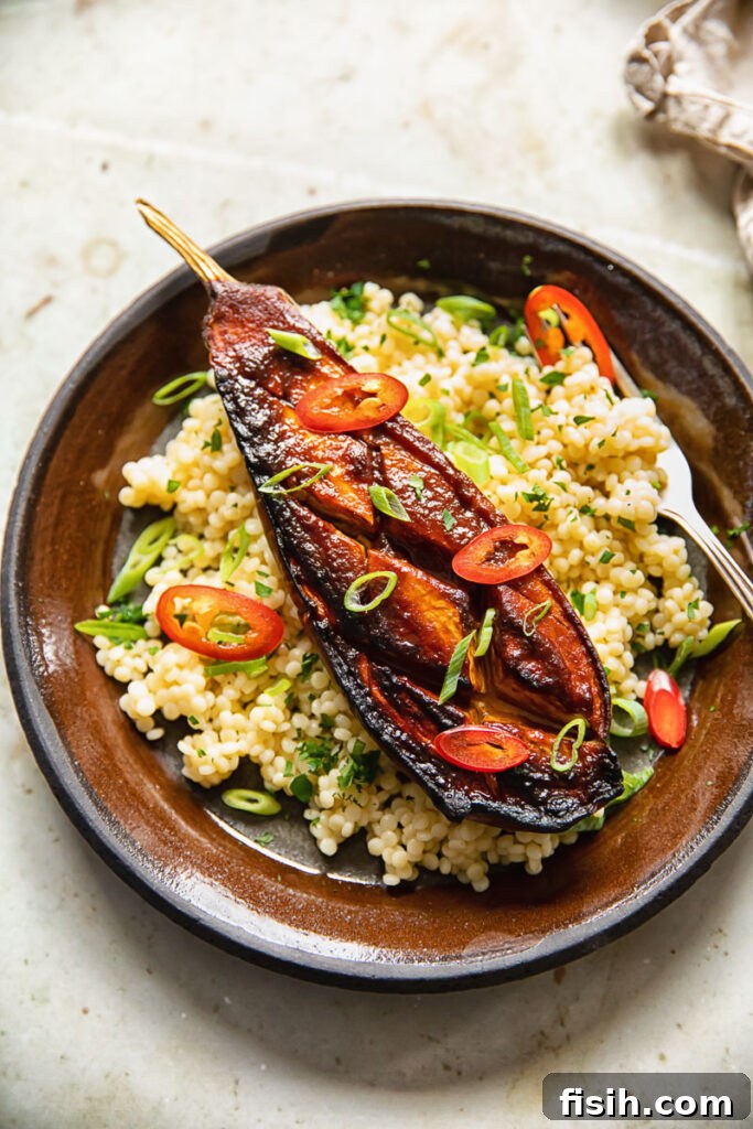 Miso-glazed aubergine served on a bed of couscous, garnished with chopped scallions.