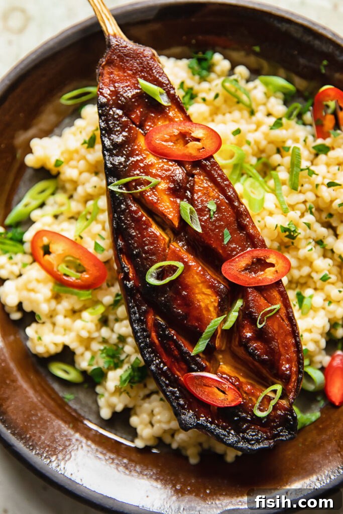 Close-up of a miso aubergine on a plate, presented with couscous and garnished with fresh herbs.