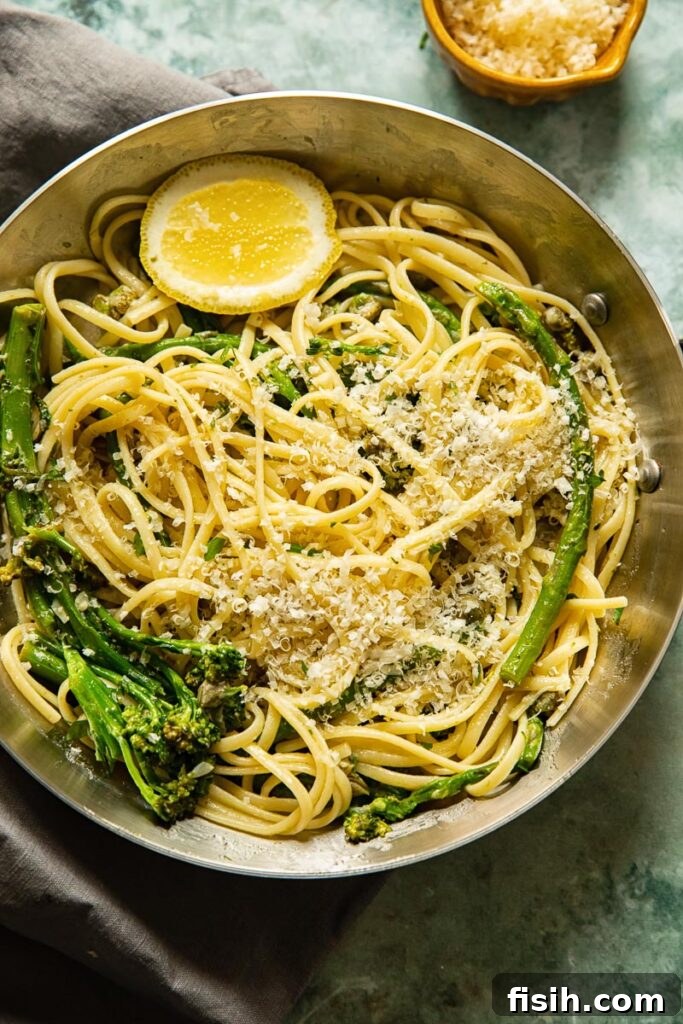 A large pan filled with the completed Lemon Garlic Pasta, topped with grated Parmesan cheese, fresh broccoli, and asparagus, ready to be served.