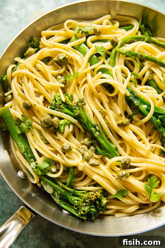 A stainless steel frying pan showcasing the freshly cooked linguine, vibrant broccoli, crisp asparagus, and salty capers, coated in a light lemon garlic sauce.