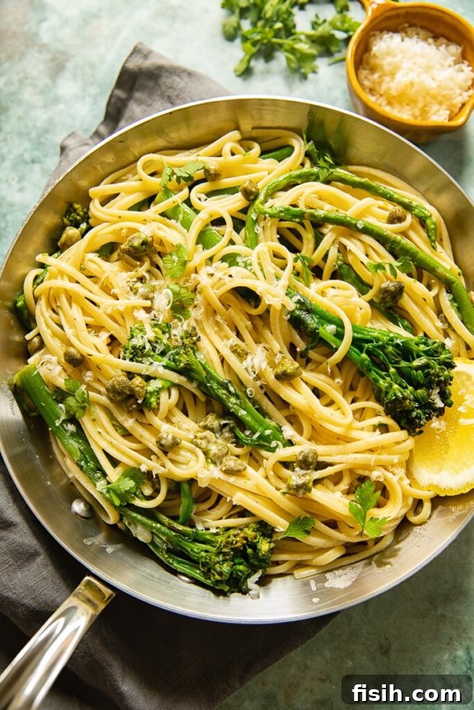 A top-down shot of a frying pan filled with Lemon Garlic Pasta, featuring linguine, broccoli, asparagus, and a light dusting of grated cheese.