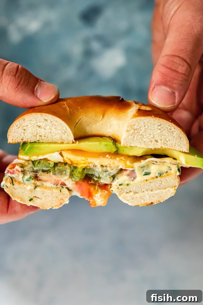 Hands holding halved bagel sandwich showing cross-section