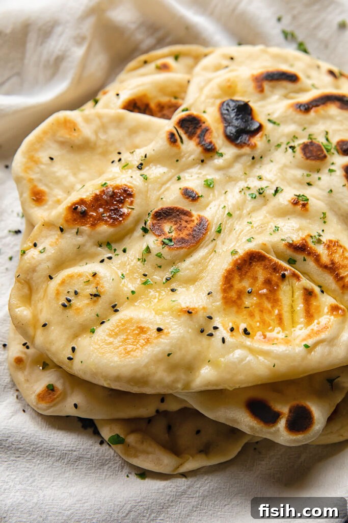 Close up shot of homemade naans stacked on top of each other and topped with garlic butter, showcasing their soft, bubbly texture.