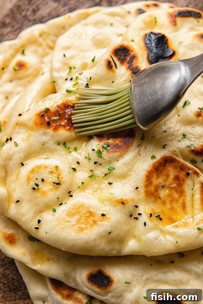 Close up shot of warm garlic butter being spread on a homemade naan with a brush, illustrating a delicious flavoring option.