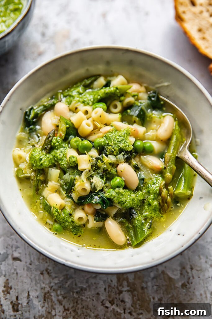 A vibrant bowl of vegetarian Spring Minestrone Soup, garnished with fresh herbs and a spoon, ready to be enjoyed.