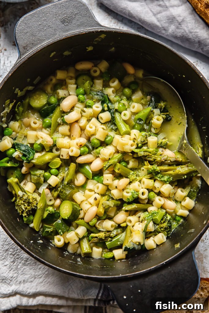 An overhead view of a large pot filled with vibrant green Spring Minestrone Soup, showcasing its fresh ingredients.
