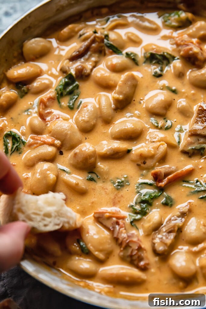 Close up shot of a piece of bread being dipped into tuscan butter beans sauce