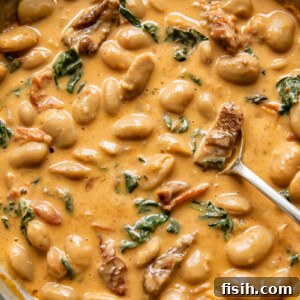 Top down shot of Tuscan butter beans in creamy sun dried tomato sauce in a pan with spinach