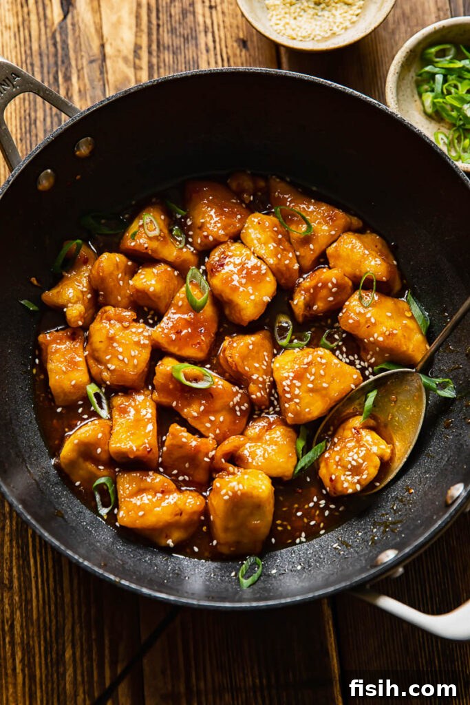 Top down view of honey sesame chicken in a wok with green onions and sesame seeds.
