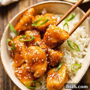 Chopsticks removing a piece of honey sesame chicken from a bowl of rice