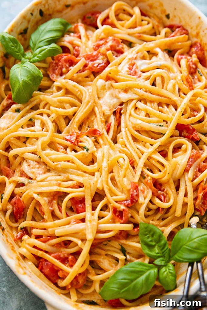 A vibrant close-up of cherry tomato pasta nestled in a baking dish, adorned with generous dollops of melted burrata, showcasing the creamy texture and rich colours of the dish.