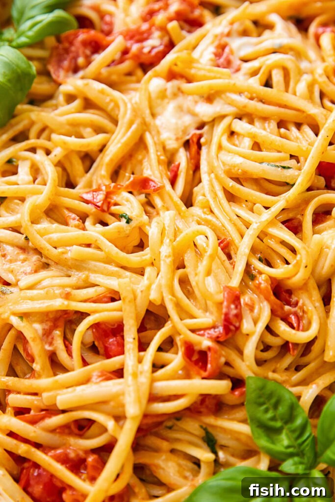 An inviting close-up of creamy cherry tomato pasta, generously garnished with vibrant green basil leaves, highlighting the freshness and rich texture of the dish.