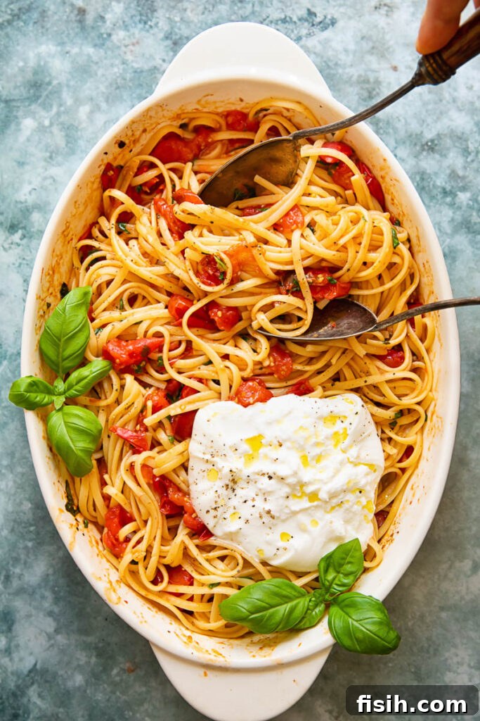 A elegant serving dish filled with roasted cherry tomato pasta and creamy burrata, accompanied by serving spoons, ready to be enjoyed.