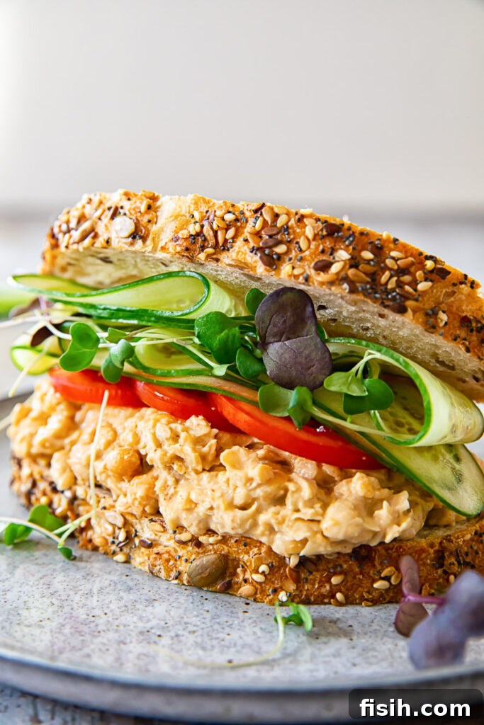 Smashed Chickpea Sandwich 2 Angled view of a vibrant chickpea salad sandwich on a plate, showcasing fresh ingredients and a golden-brown bread.