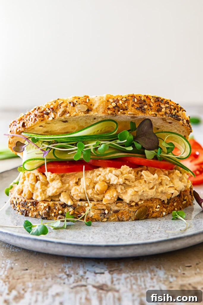 Smashed Chickpea Sandwich 5 A front view of a richly loaded chickpea salad sandwich, brimming with fresh vegetables and the creamy chickpea filling.