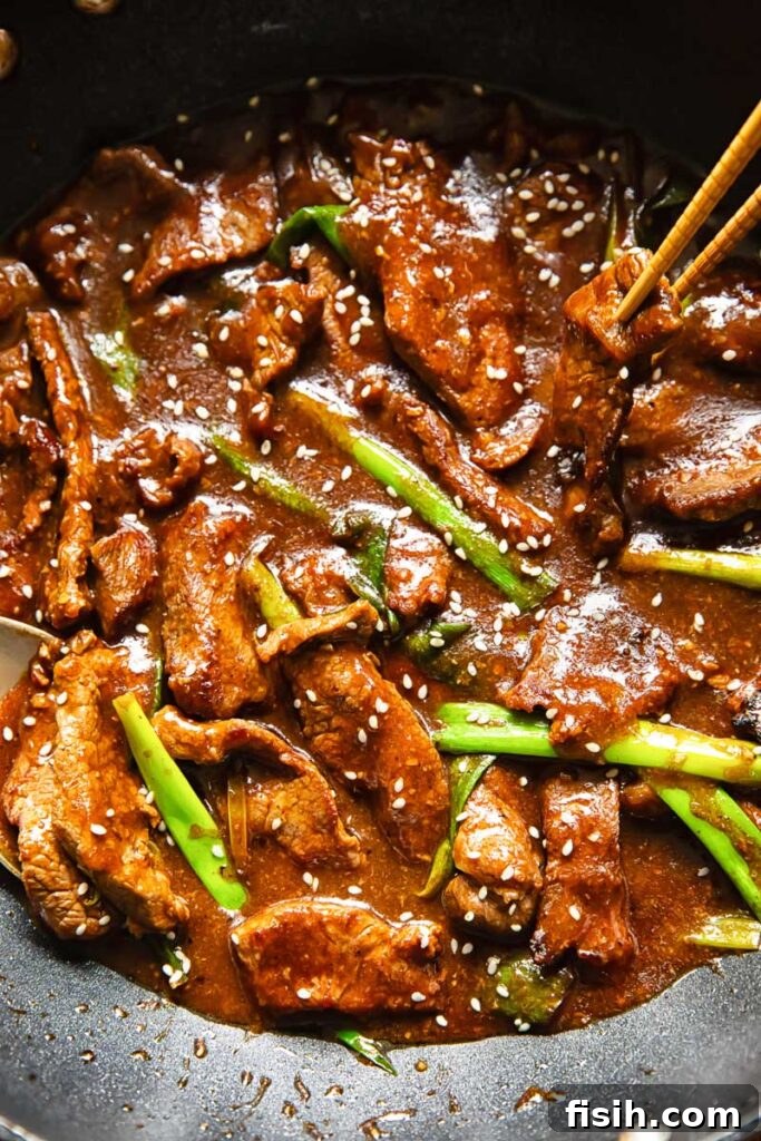 Top down shot of beef strips and green onion stir fry in a pan topped with sesame seeds