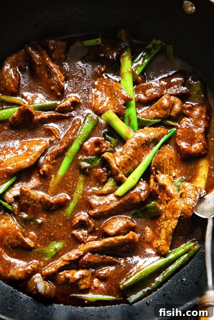 Close up shot of Mongolian beef with green onions and sesame seeds in a pan