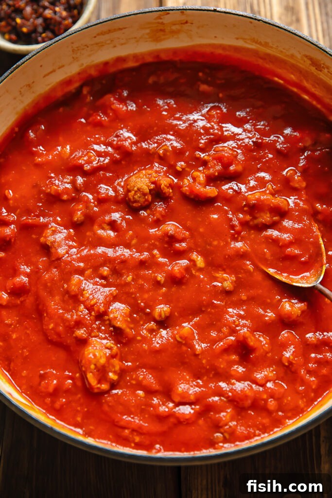 Top down shot of sausage ragu tomato sauce in a large pan with a serving spoon