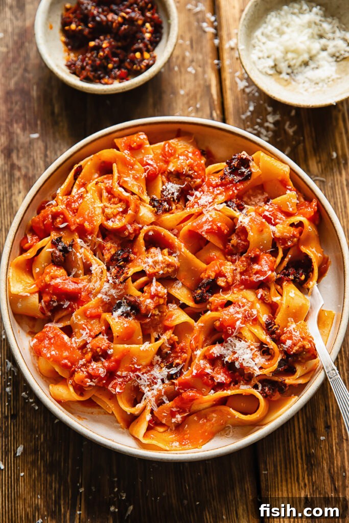Top down shot of chilli crisp sausage ragu in a bowl with a fork topped with Parmesan