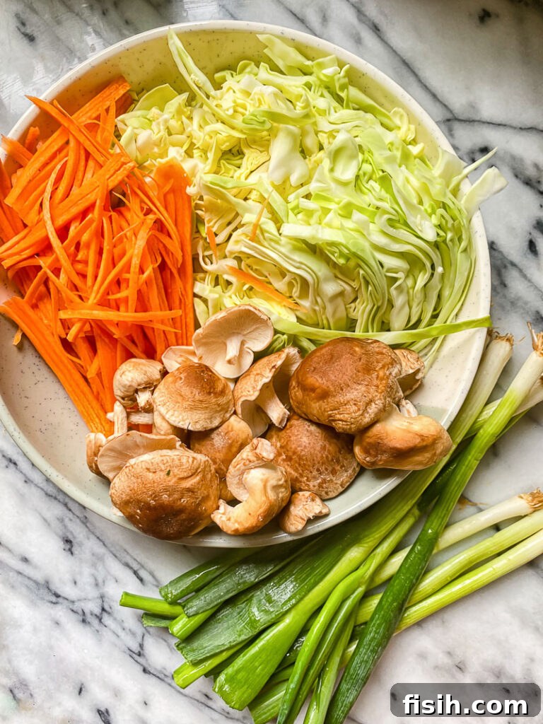 Vegetarian Yaki Udon Stir-Fry 4 Raw ingredients for yaki udon laid out on a plate: julienned carrots, thinly sliced cabbage, whole shiitake mushrooms, and fresh green onions.