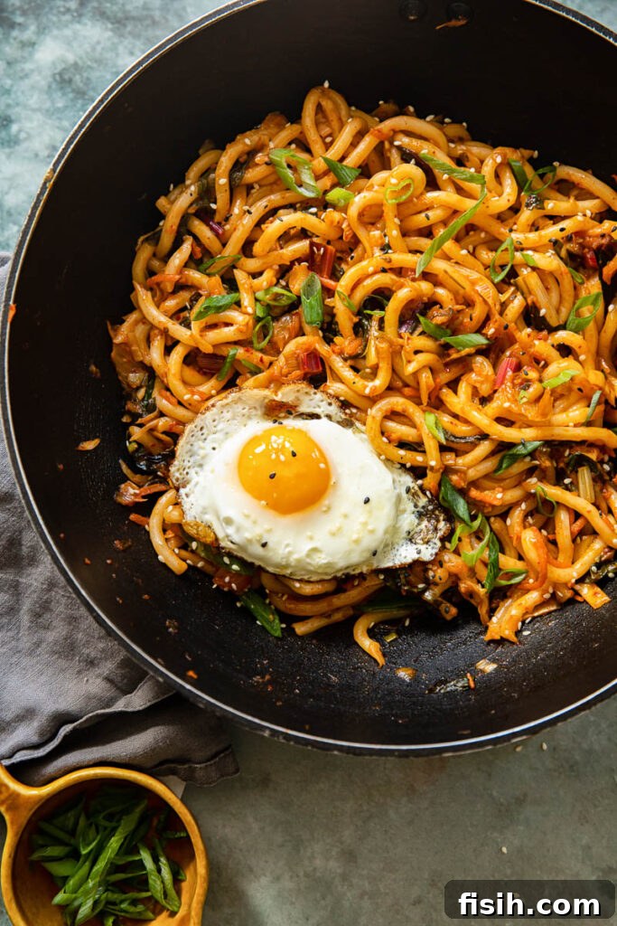 Kimchi Noodles in Minutes 3 Kimchi noodles being stir-fried in a wok-style pan, with a fried egg resting on top, showcasing the vibrant ingredients