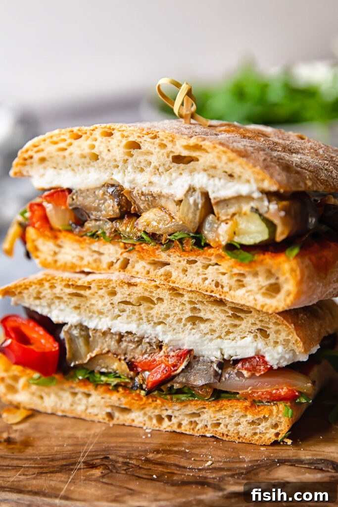 Harvest Roasted Vegetable and Creamy Chevre Sandwich 2 A vibrant and appetizing close-up profile of a Roasted Vegetable and Goat Cheese Sandwich, showcasing layers of colorful roasted vegetables, creamy goat cheese, and fresh greens on ciabatta bread.