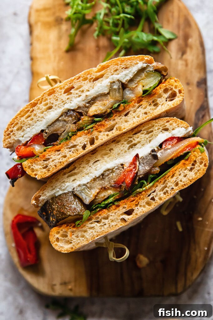 Harvest Roasted Vegetable and Creamy Chevre Sandwich 4 A close-up side view of the perfectly assembled Roasted Vegetable and Goat Cheese Sandwich, cut in half and presented on a rustic cutting board.