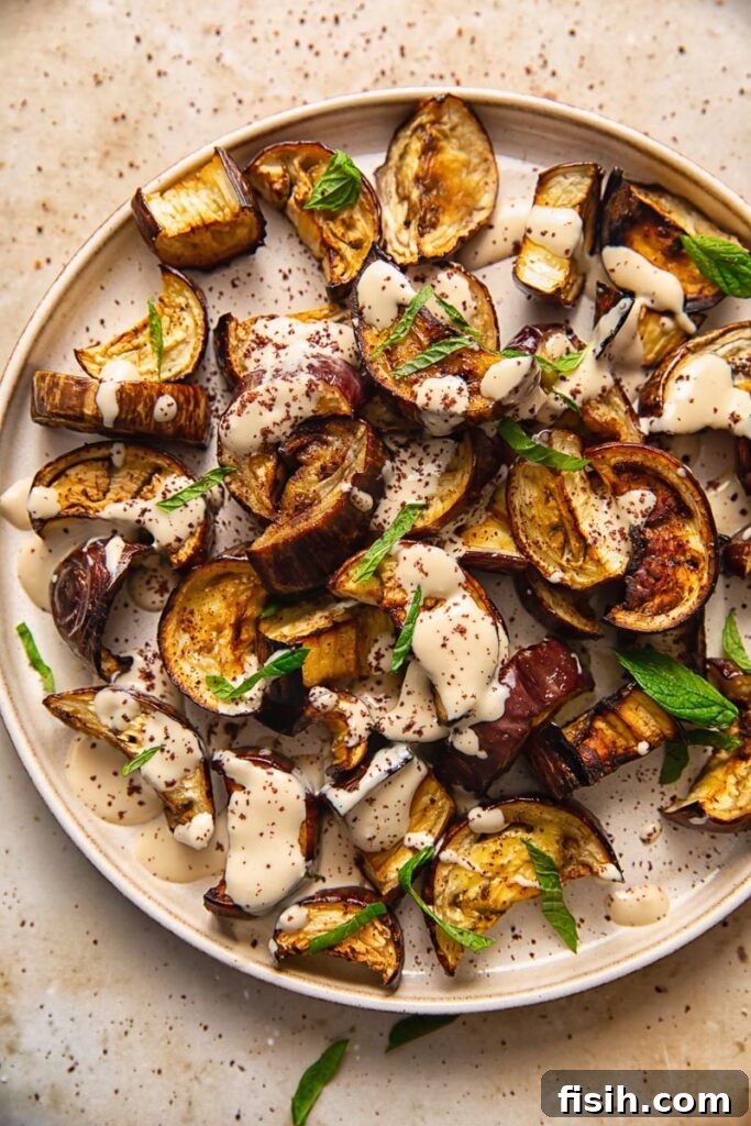 Tahini-Kissed Roasted Eggplant with Garlic 2 Close up of perfectly roasted aubergine slices on a plate, drizzled with creamy tahini sauce and garnished with fresh mint leaves.