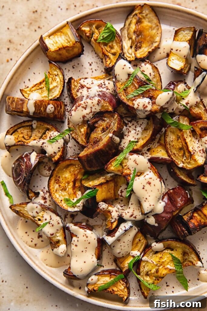 Tahini-Kissed Roasted Eggplant with Garlic 3 A close-up view of roasted aubergine on a pristine white plate, generously coated with a smooth tahini sauce.