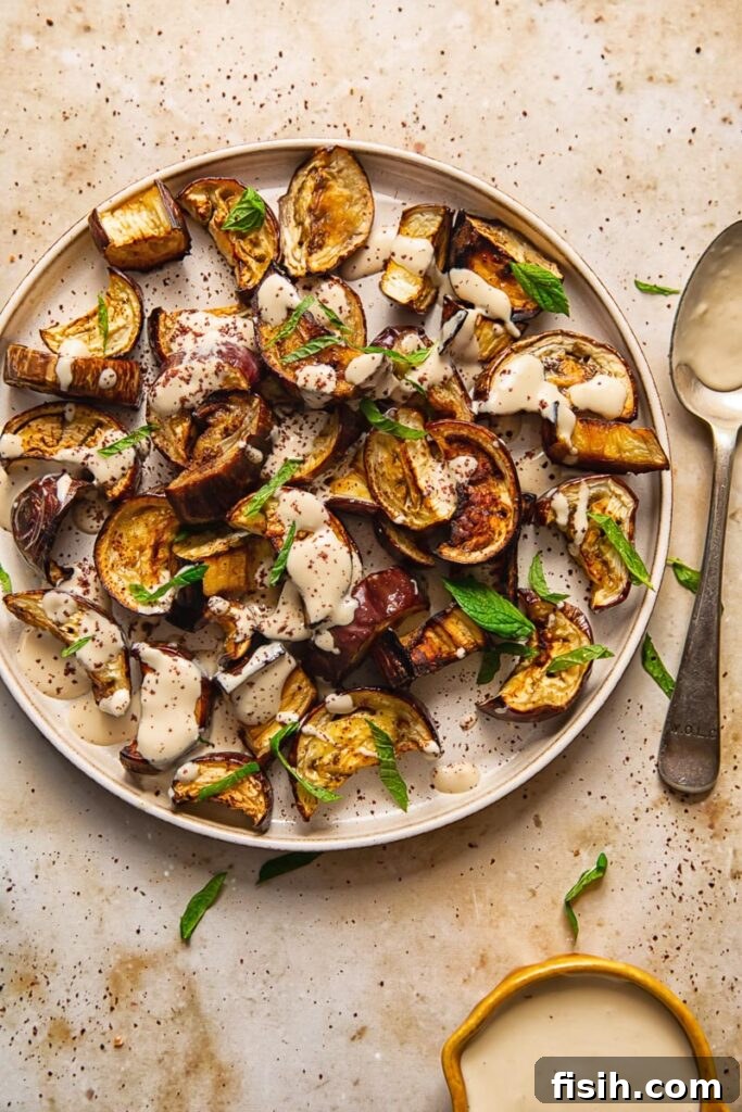 Tahini-Kissed Roasted Eggplant with Garlic 6 A plate of golden roasted aubergine next to a spoon, with a small bowl of extra tahini sauce ready for serving.