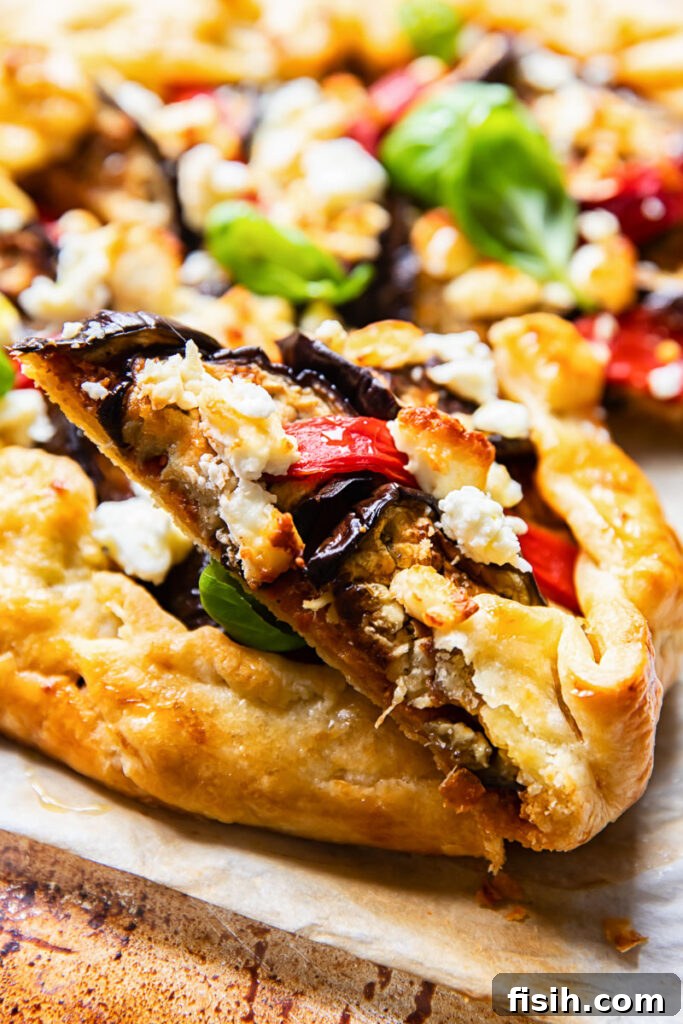 Close-up side view of a slice of savory galette, revealing the layers of eggplant, red pepper, and feta.