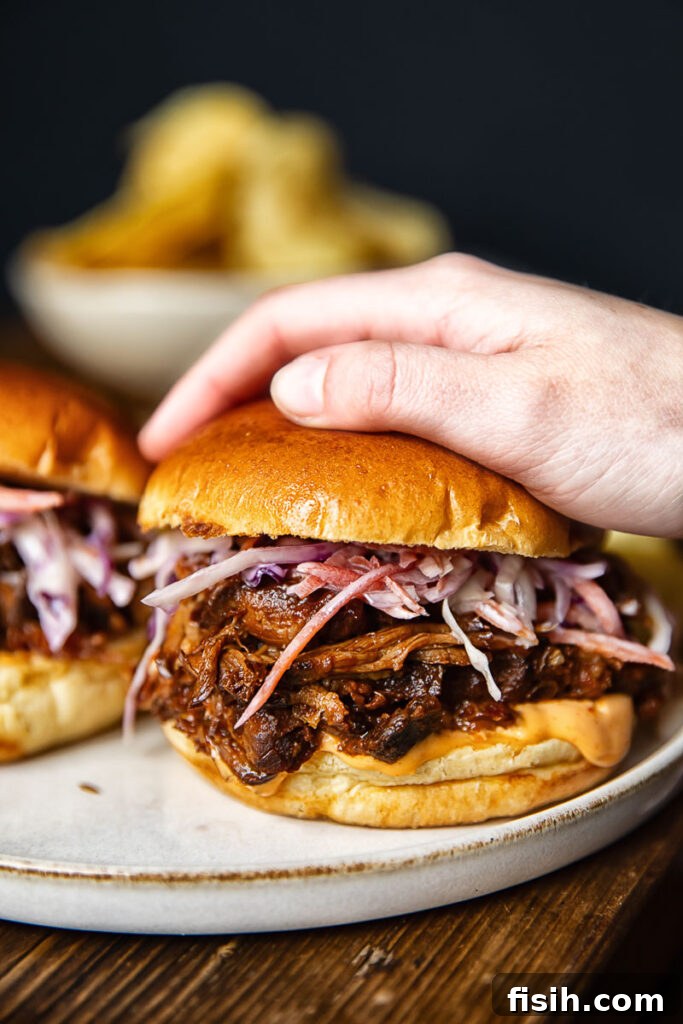 Pulled Pork Sandwich Delights 4 Side shot of someone picking up a pulled pork sandwich off of a plate next to another sandwich