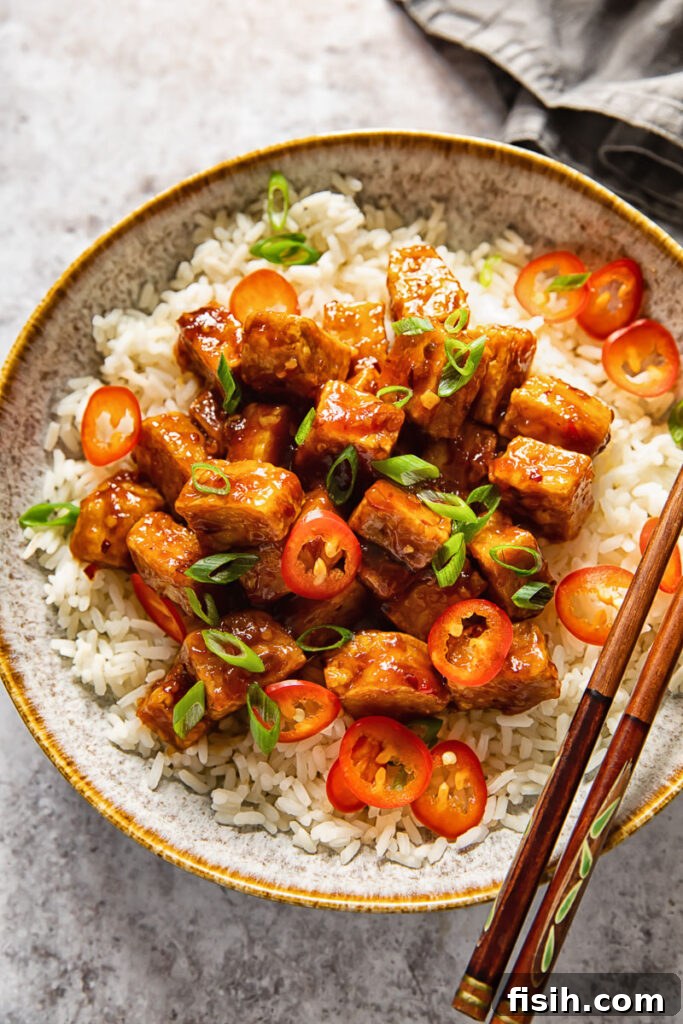 bowl of rice topped with tofu and two chopsticks