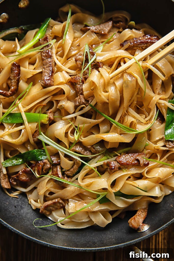 Top down shot of chop sticks picking up chow fun noodles with beef and beansprouts from a pan