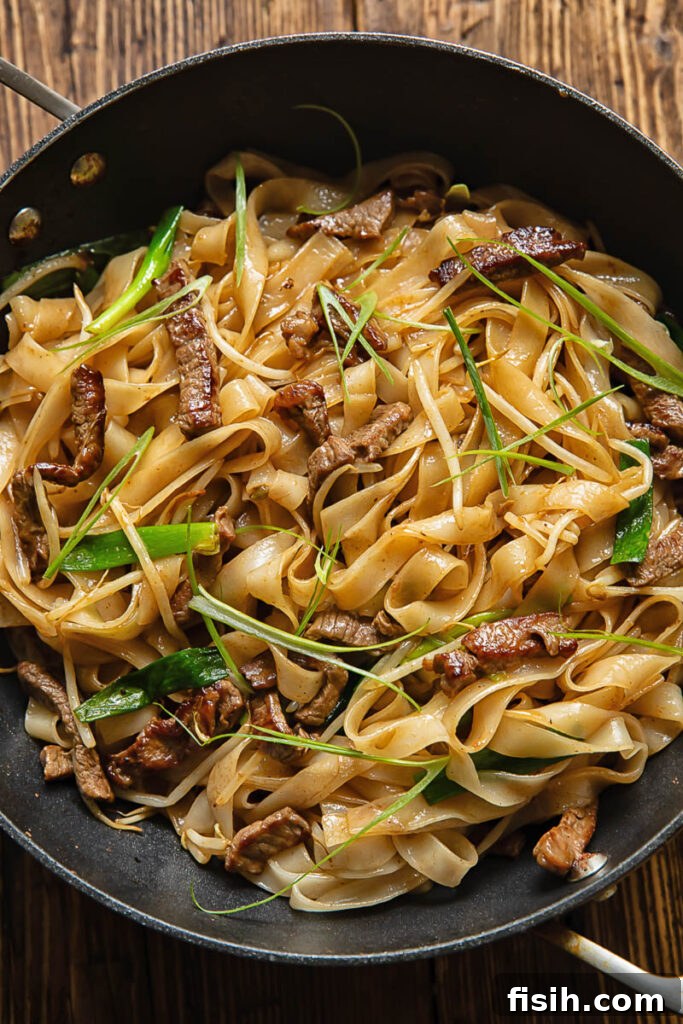 Top down shot of chow fun stir fry noodles in a large pan