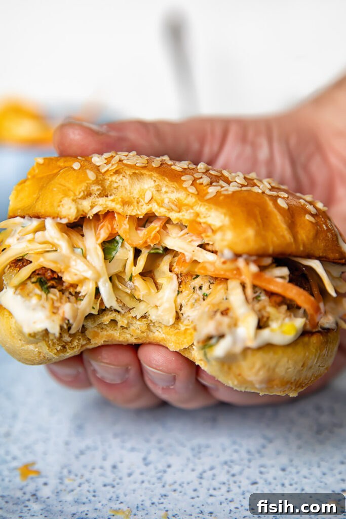 Close up shot of hand holding a crab cake sandwich with a bite taken out of it