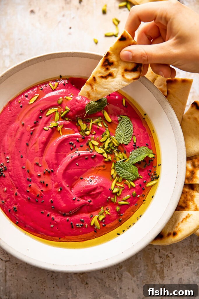 Hand reaching to dip a piece of flatbread into a bowl of creamy beetroot borani, highlighting the dip's enticing texture.
