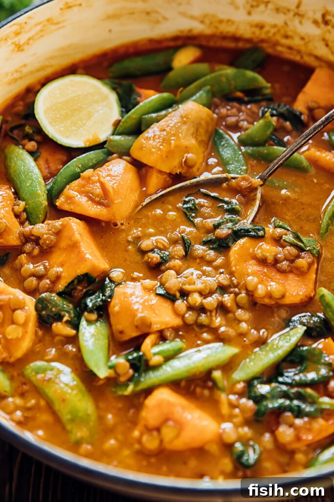 Sweet potato and lentil curry simmering in a pan with a serving spoon, showcasing its rich texture and vibrant colors.