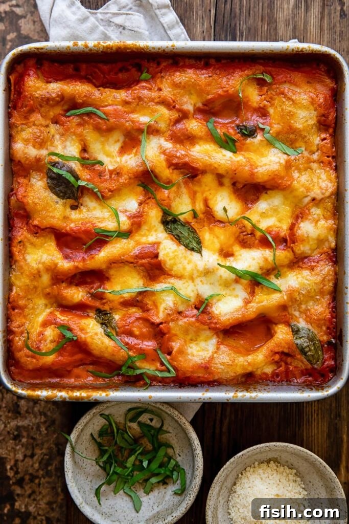 Top-down view of a baking dish filled with bubbling spinach and ricotta cannelloni, topped with melted mozzarella and fresh basil, ready to serve.