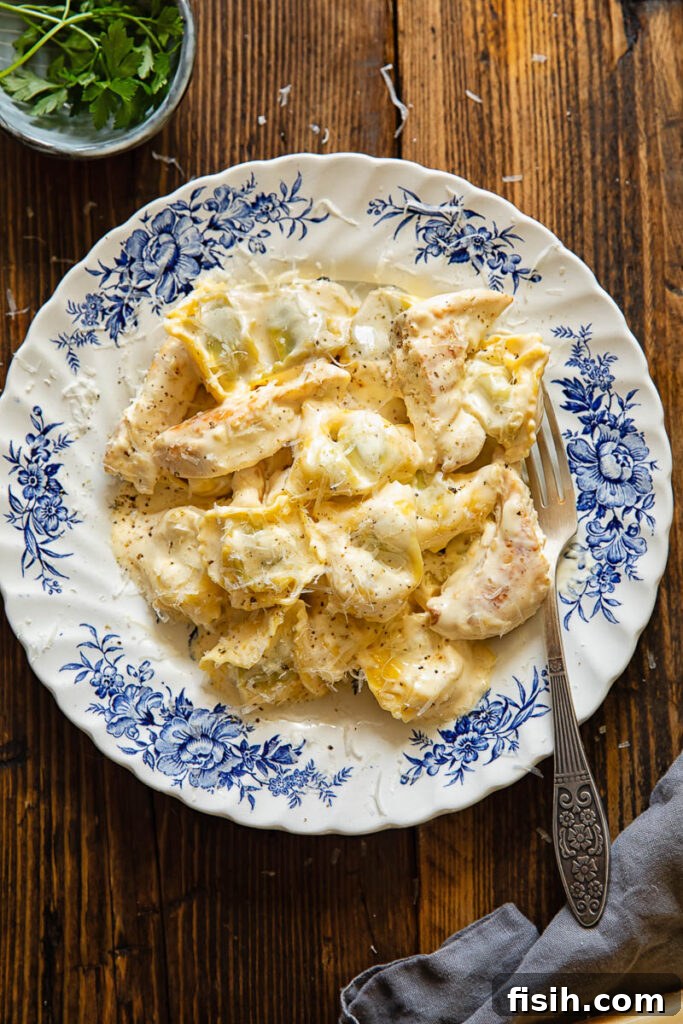 Creamy Chicken Tortellini Alfredo 4 Top down shot of a fork in a bowl of chicken tortellini alfredo next to a bowl of green herbs